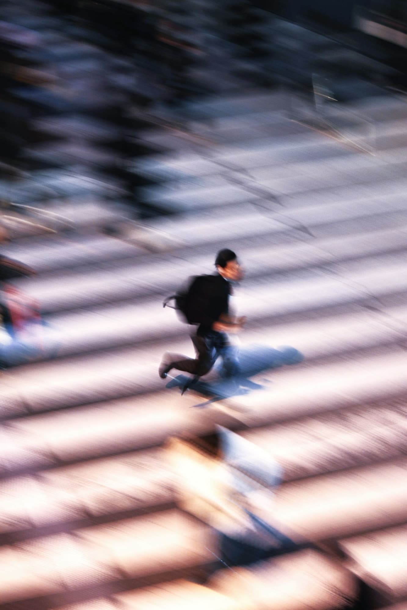 Um corredor de mochila atravessando uma escadaria larga, a imagem toda riscada pelo movimento