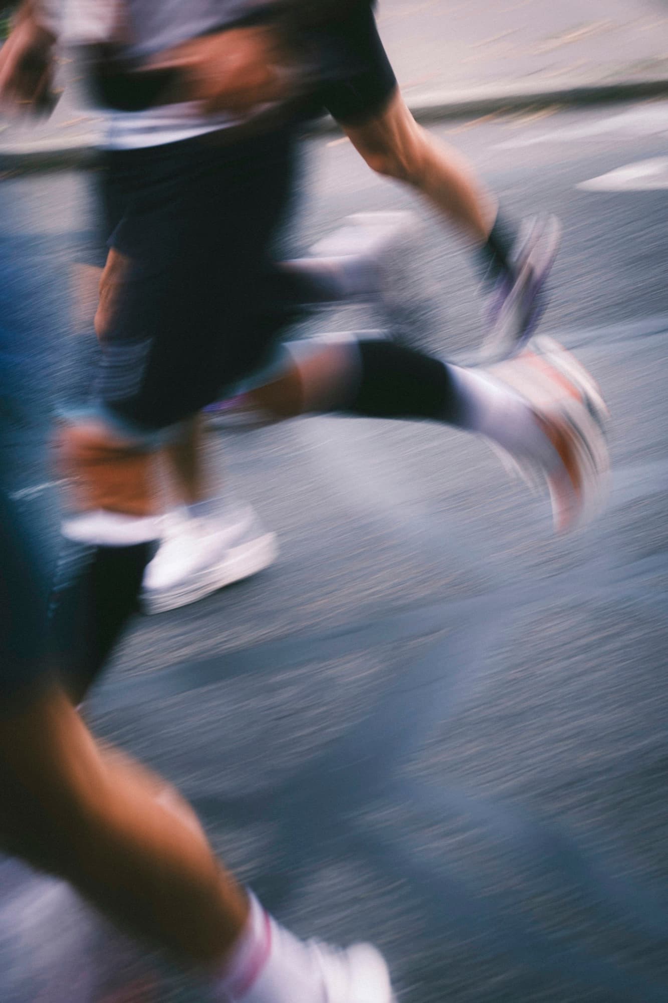 Race runners' legs and shoes, blurred by speed on a city road