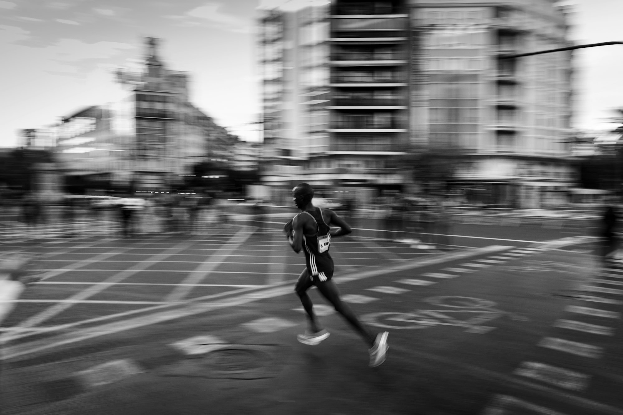 Um maratonista atravessando uma avenida, os prédios borrados pela velocidade